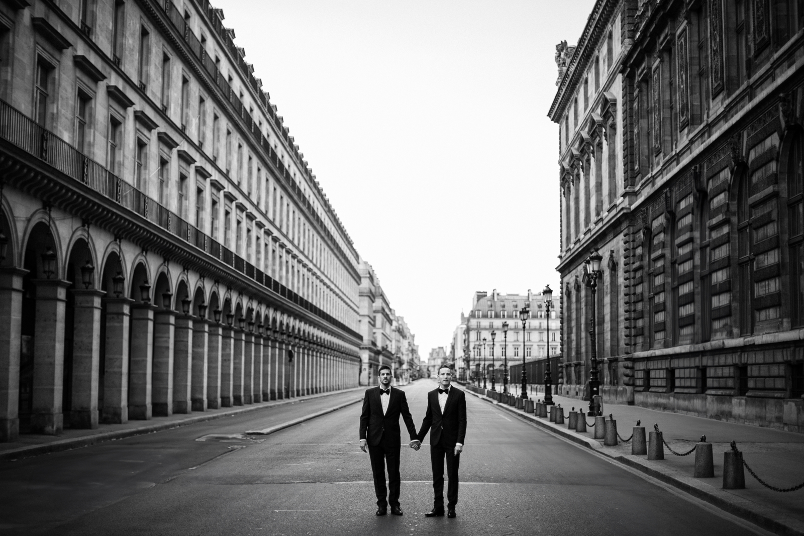 Pareja de novios de dos hombres cogidos de la mano en una calle de París. Fotografía en blanco y negro