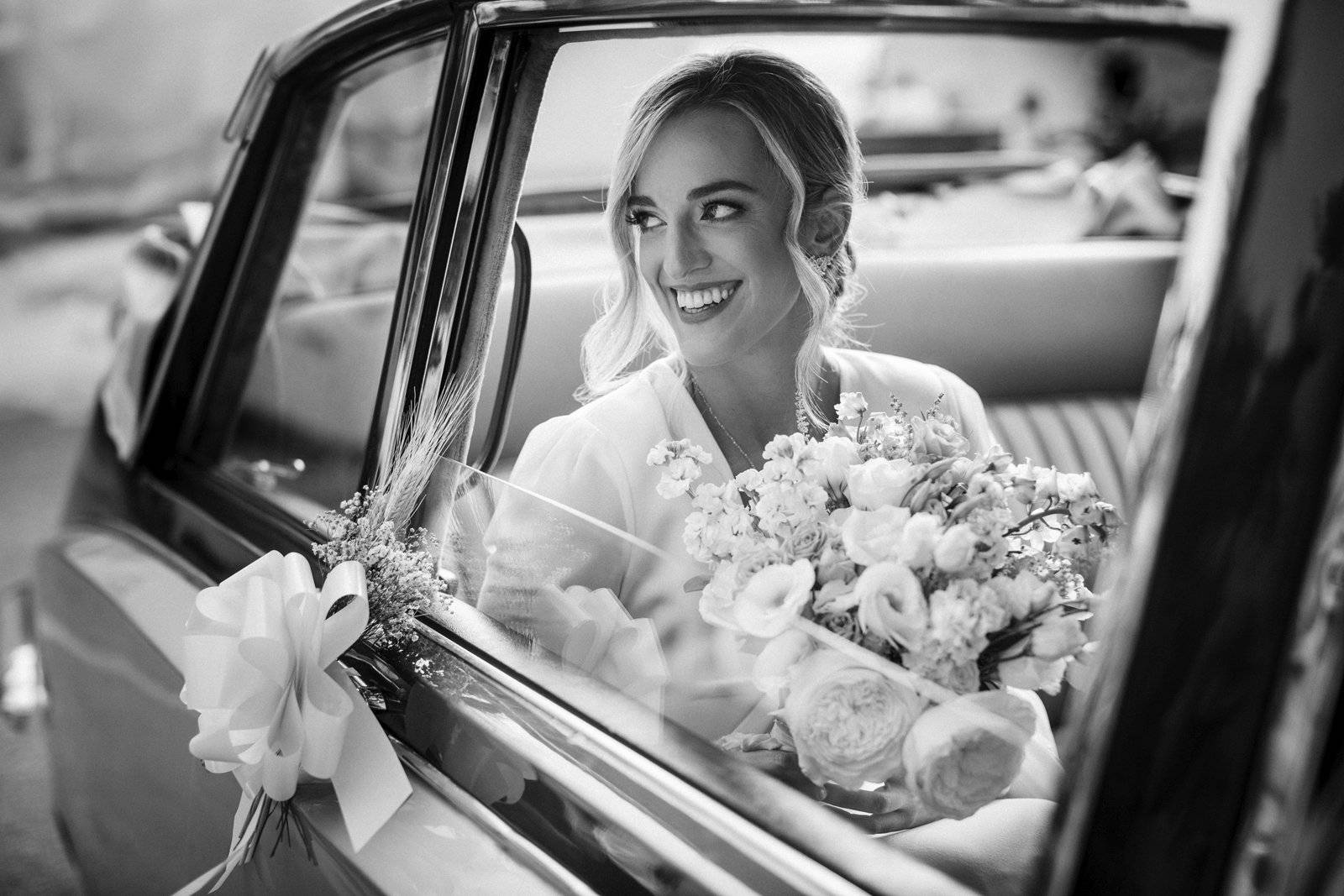 Fotografía de boda en Granada: novia en coche nupcial mirando por la ventana, vestida de blanco con ramo de novia en la mano