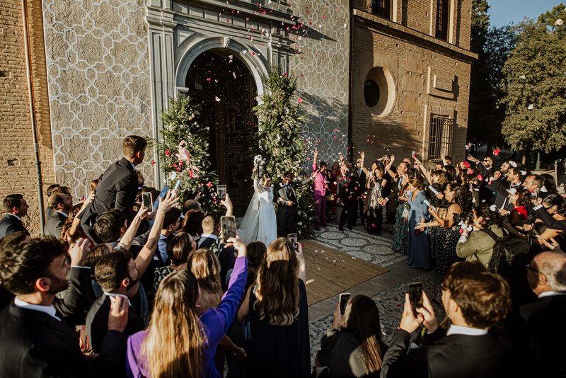 Pareja de novios saliendo de la iglesia con multitud de invitados tirándoles arroz