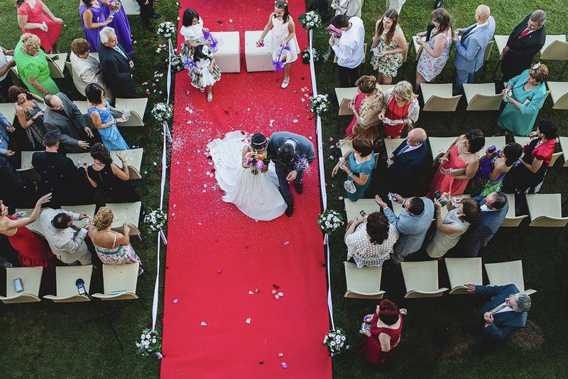 vista cenital de pareja de novios caminando por pasillo con alfombra roja, mientras los invitados les lanzan arroz