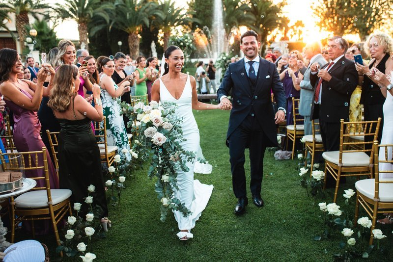 pareja de novios llegando al cóctel al aire libre, aplaudidos por los invitados
