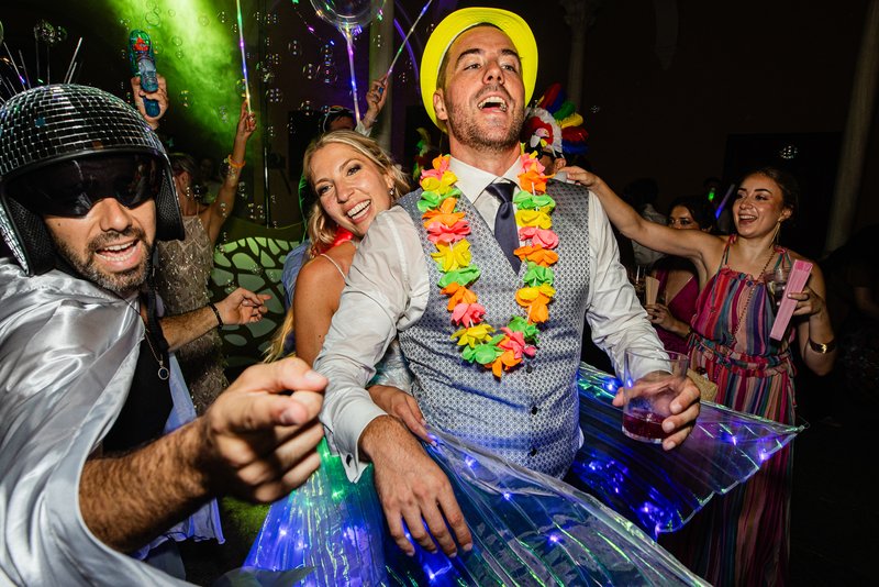 Novio de fiesta en una boda, con collar hawaiano y resto de amigos bailando