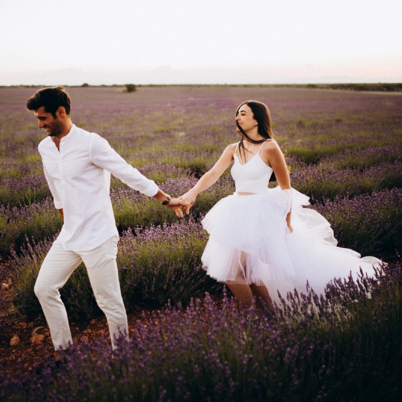 Sesión de fotos en pareja en Granada: pareja vestida de blanco correteando por el campo, cogidos de la mano