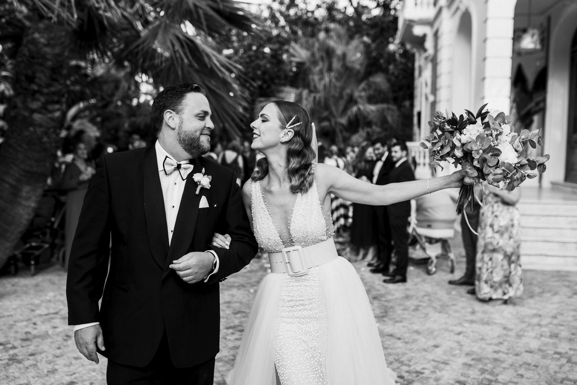 Fotografía en blanco y negro de pareja de novios cogidos del brazo, mirándose cn gesto romántico, en un jardín