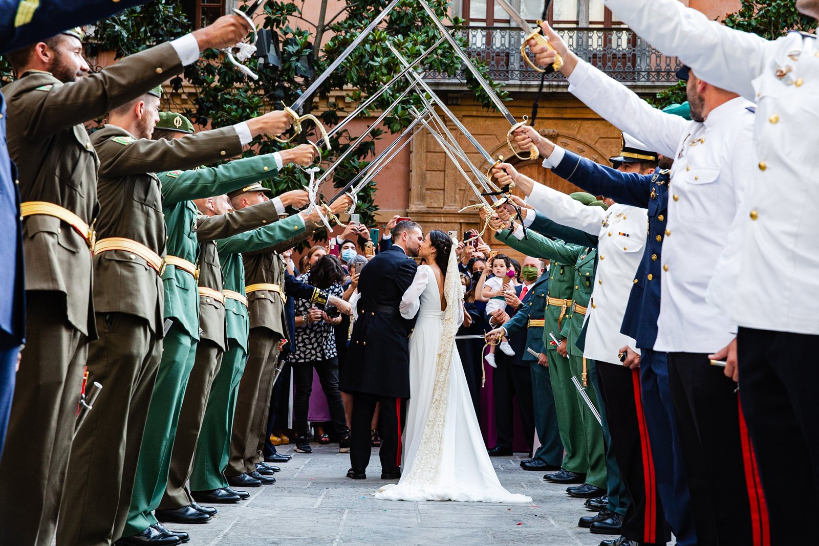 Novios besándose con una fila de militares levantando sus espadas a lado y lado, y los familiares al fondo